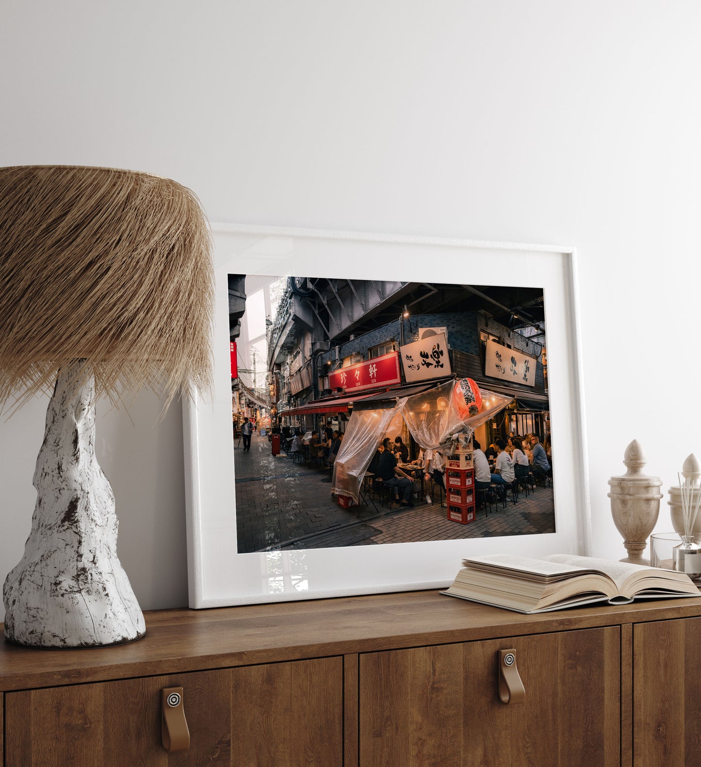 Flavors Of Ueno" framed photo leans on a wooden cabinet next to a lamp, decor, and an open book.