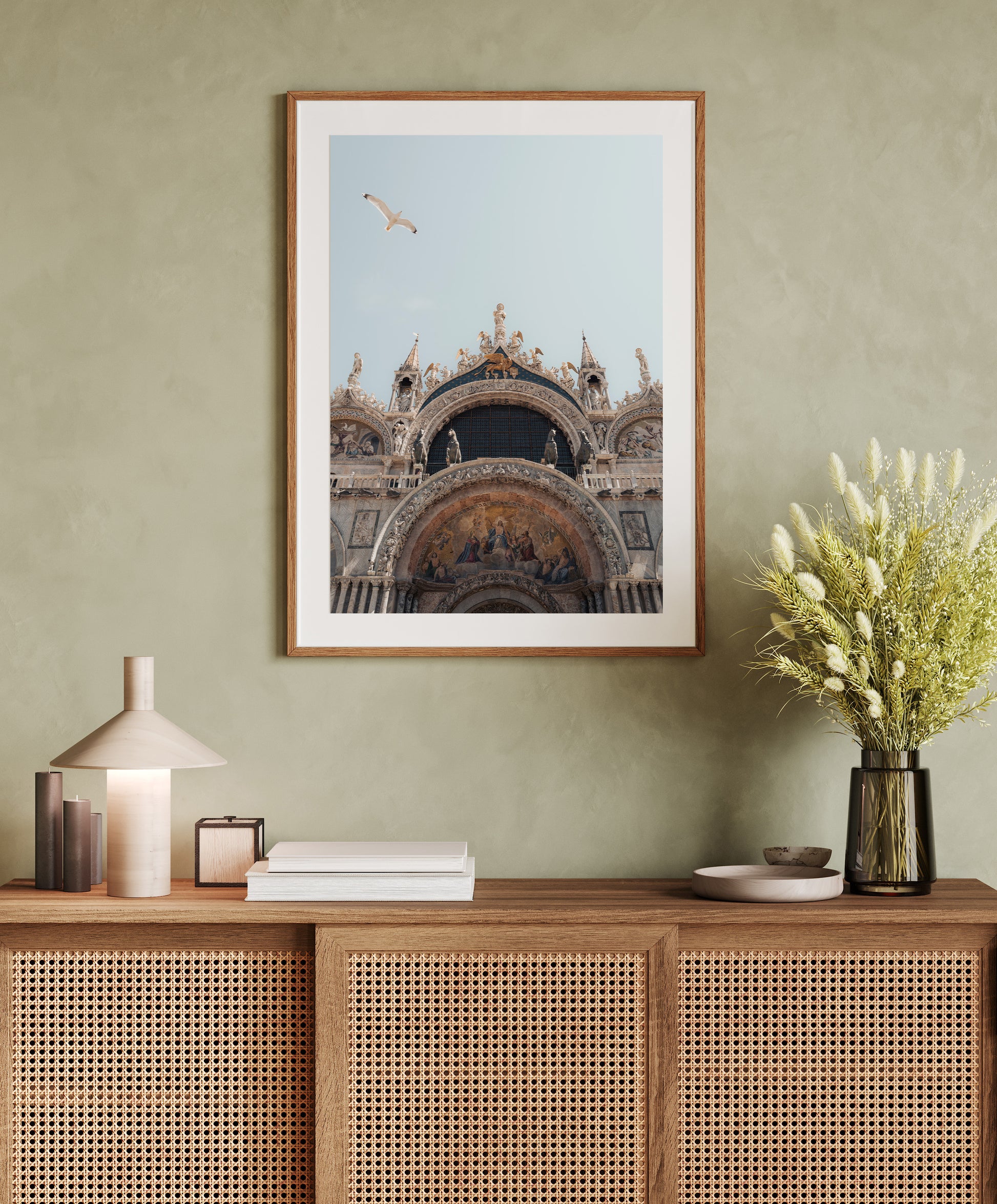 Framed photo of St. Marks Basilica above a wooden console table with books, a lamp, and a vase of flowers.