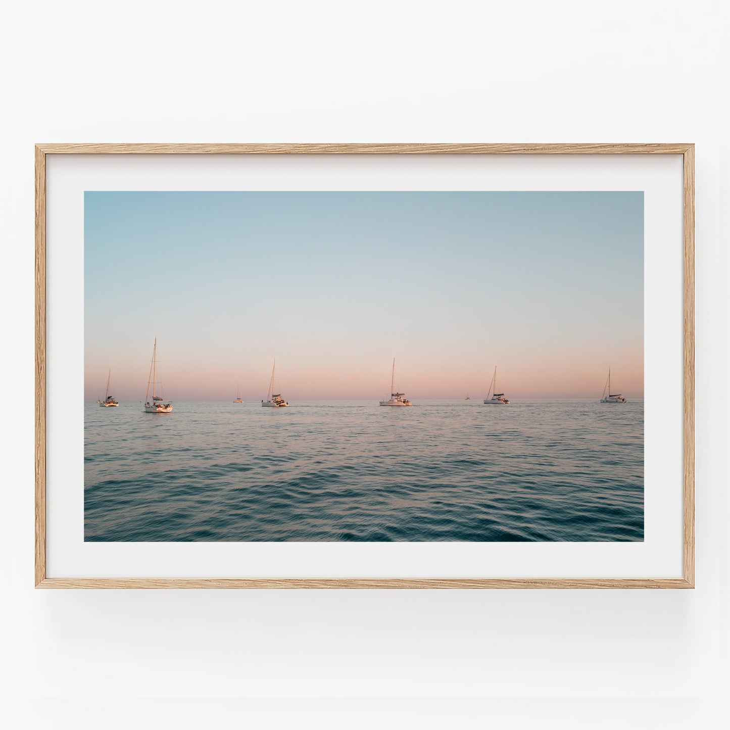 Sunset Formation—a framed photo featuring sailboats on tranquil ocean water beneath a pastel sunset sky.