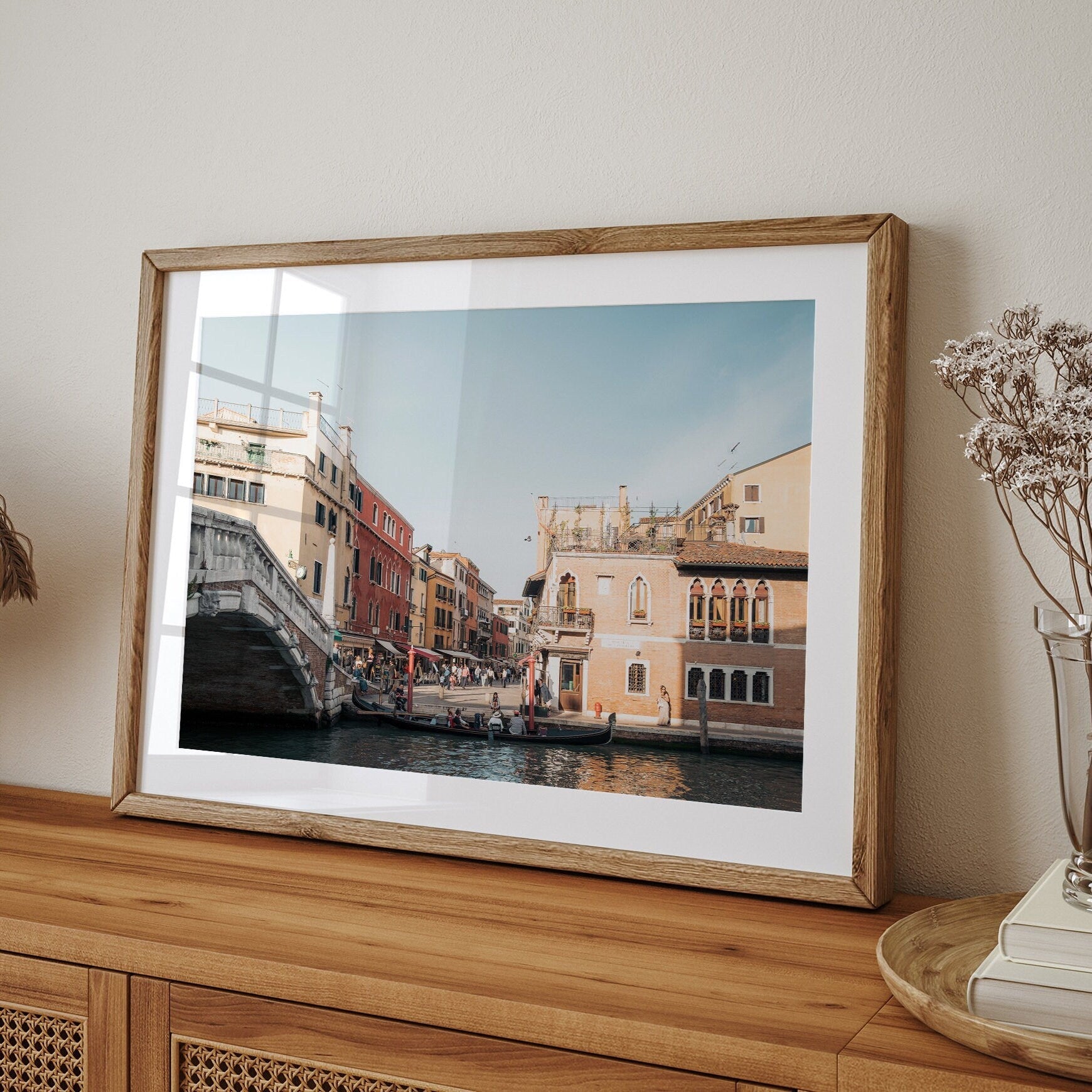 A Day in Venice framed photo on a wooden cabinet, with a vase of dried flowers nearby.
