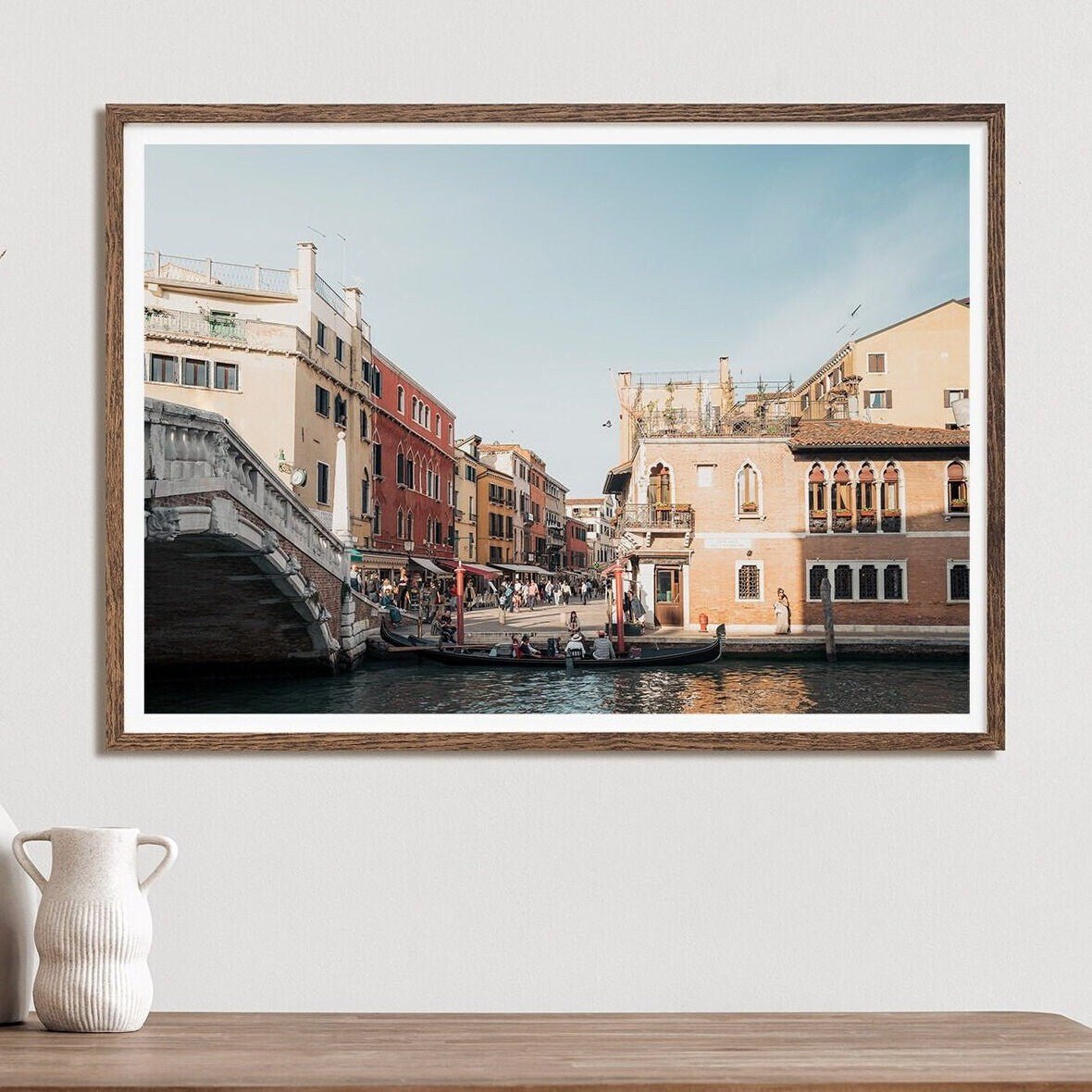 The framed photo, A Day in Venice, showcases a canal with historic buildings and a stone bridge on a wooden surface.