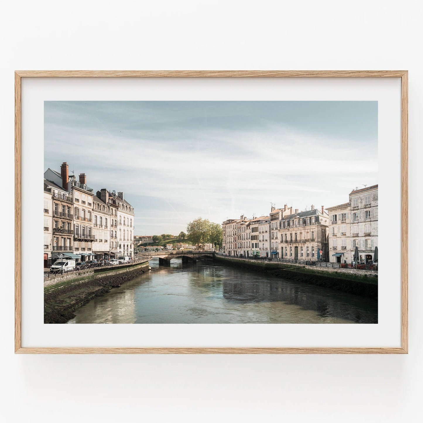 A framed photo titled Adour River featuring a scenic European canal with historic buildings under a clear sky.