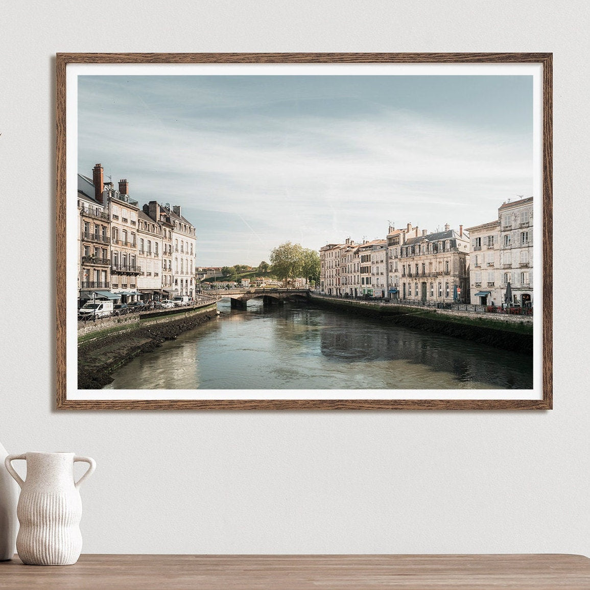 The Adour River framed photo shows a riverside cityscape above a ceramic vase on the wall.