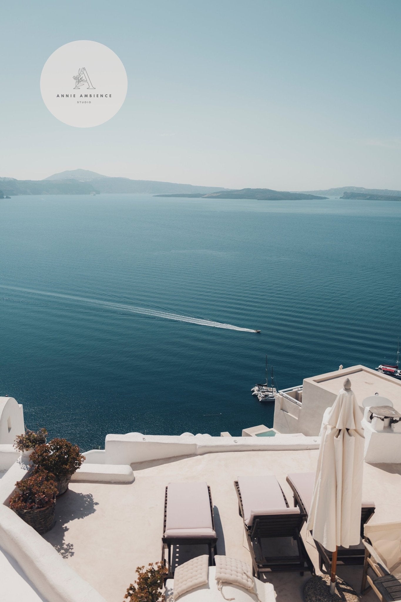 Aegean Escape: Serene coast, blue waters, distant boat, sun loungers on white terrace. Logo top left.