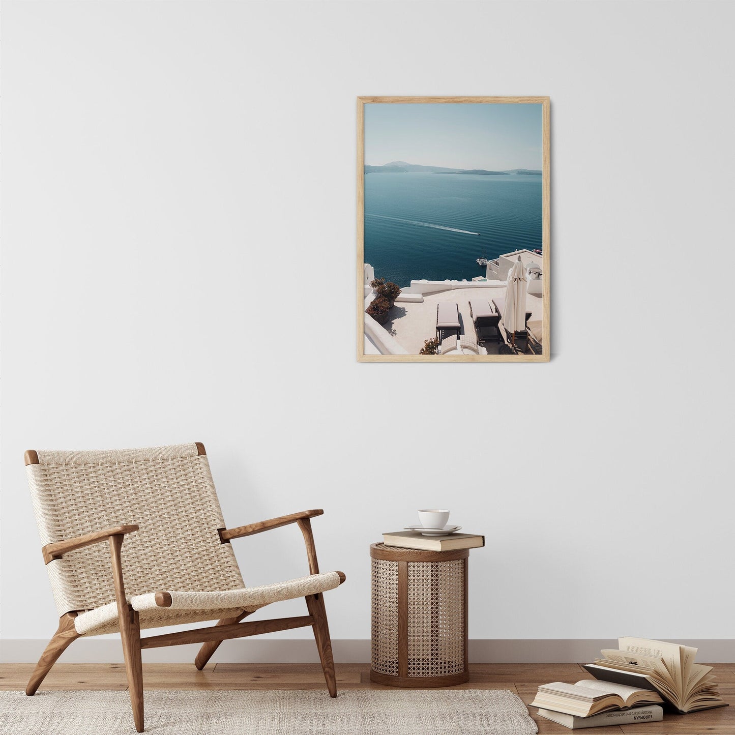 A cozy room featuring the Aegean Escape framed photo, wicker chair, side table, and open books.