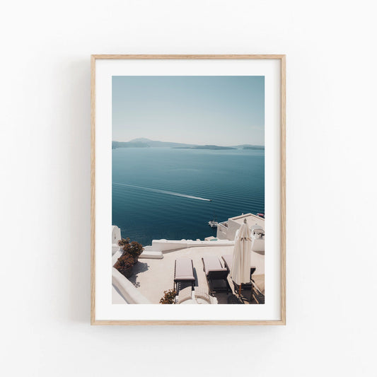 Framed Aegean Escape photo: serene seaside with white buildings, lounge chairs, and a boat.