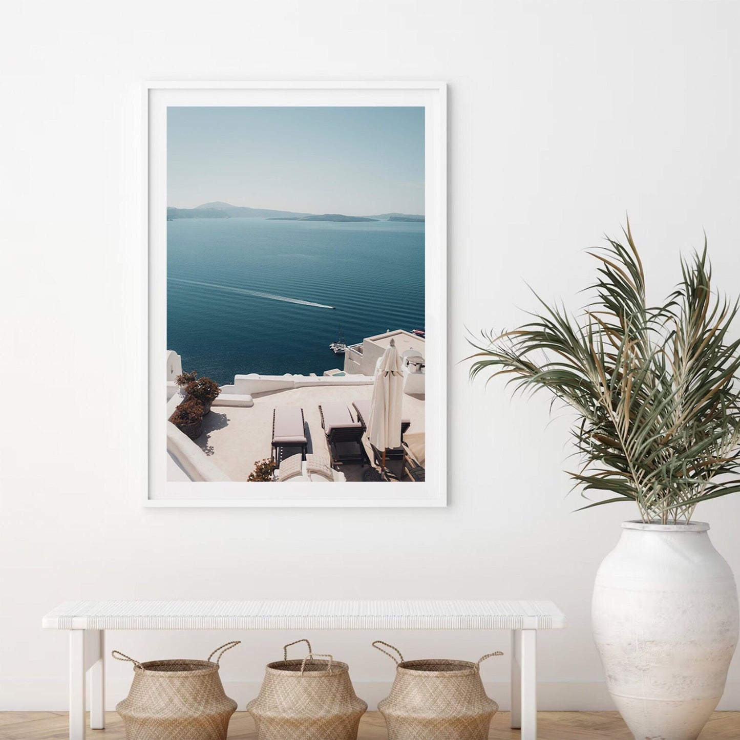 Aegean Escape photo on a white wall, with a bench, plant below, and baskets on the floor.