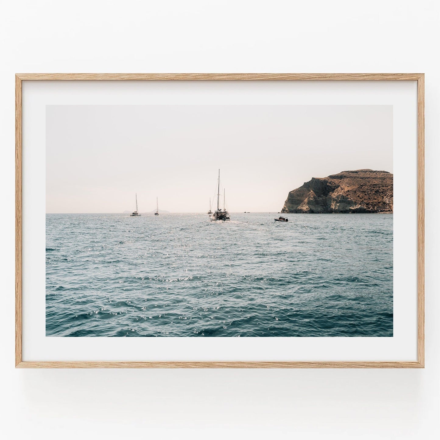 Afternoon Sail II features sailboats on a calm sea near rocks, framed in light wood against a plain white background.