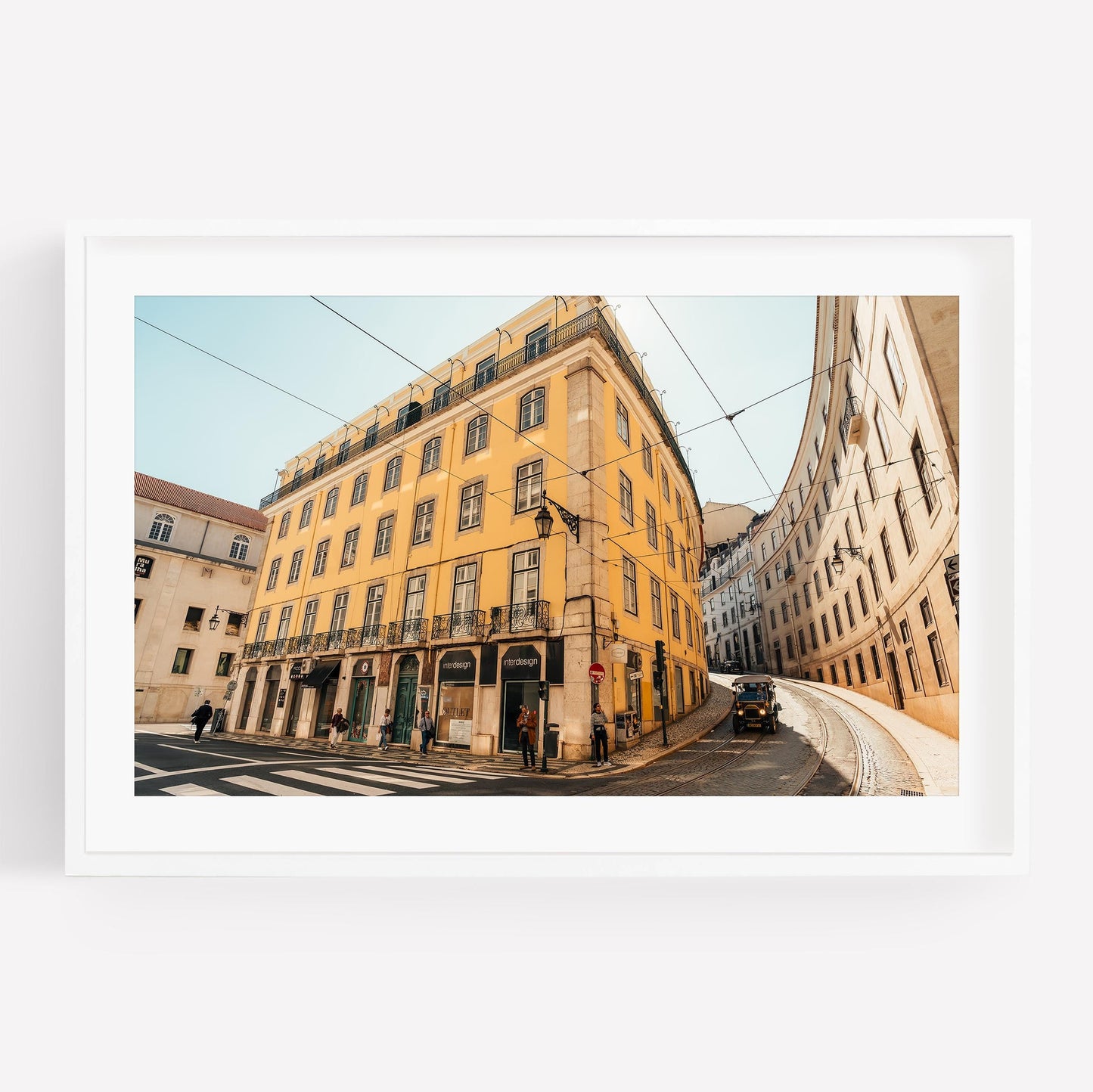Framed photo of Baixa-Chiado: yellow building on curved street with people and tram tracks under a clear sky.