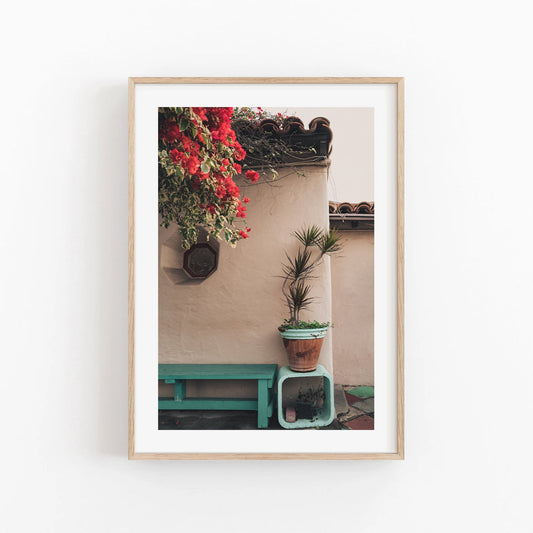The Balboa Charm features a photo of potted plants, red flowers, and a bench by a stucco wall with weathered roof tiles.