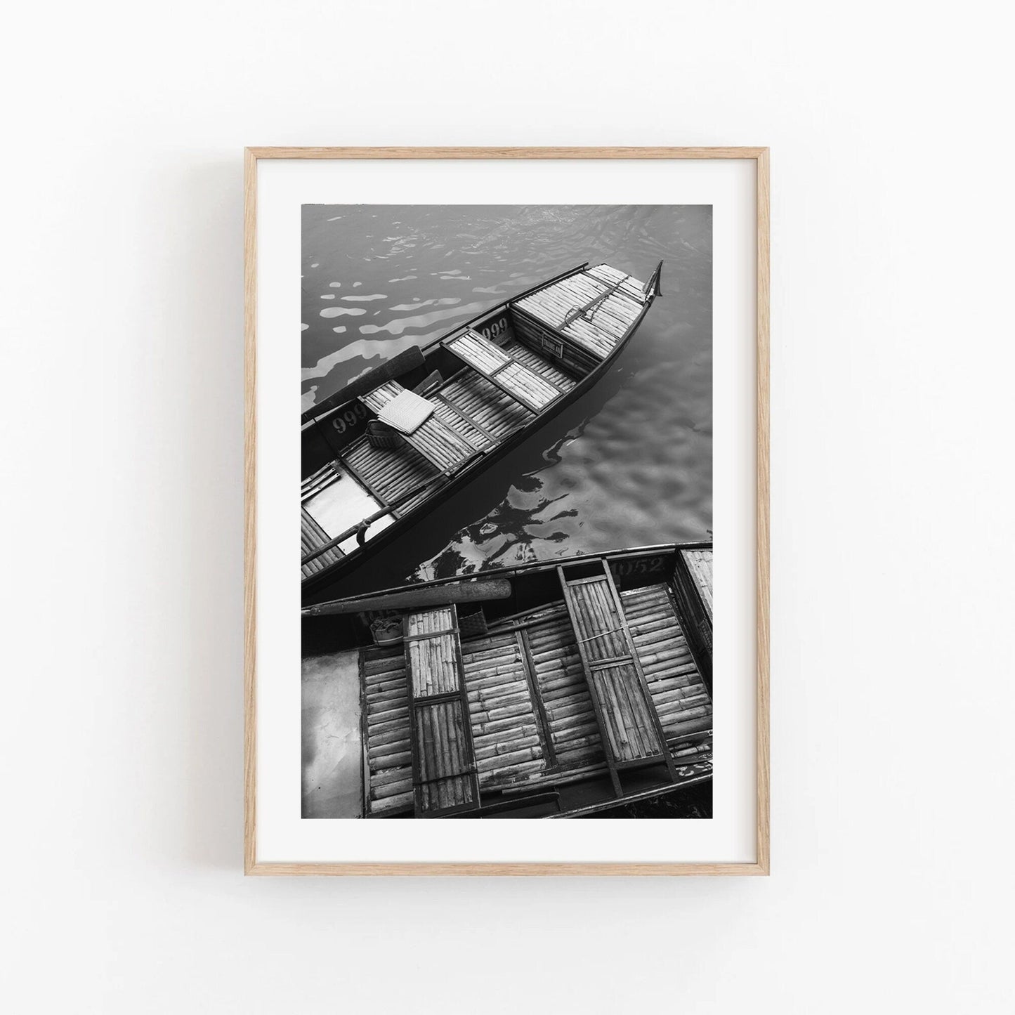 Bamboo Boat I Black and White, a framed photo of two wooden boats on calm water in light wood.
