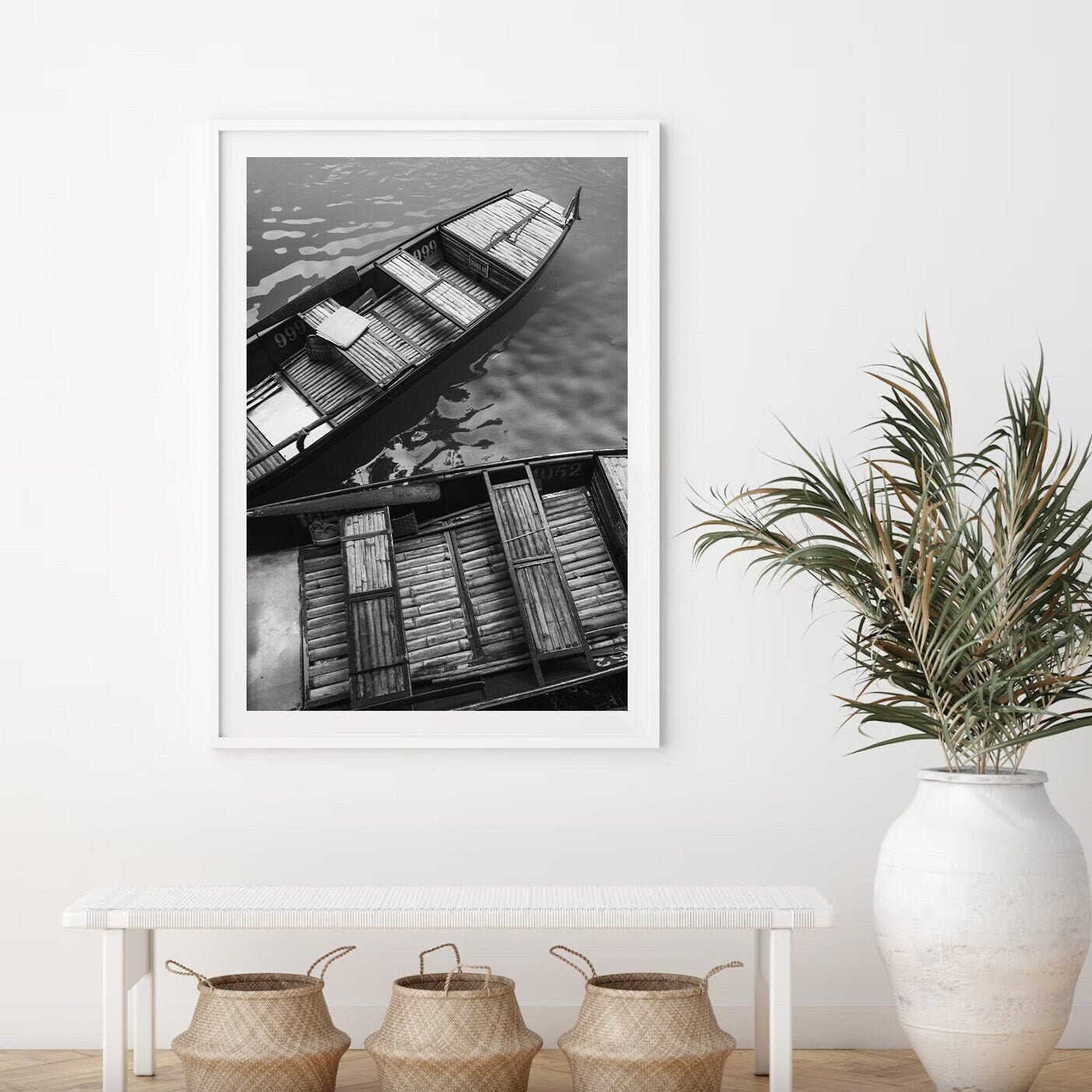 Framed Bamboo Boat I Black and White photo hangs above a bench on a white wall.