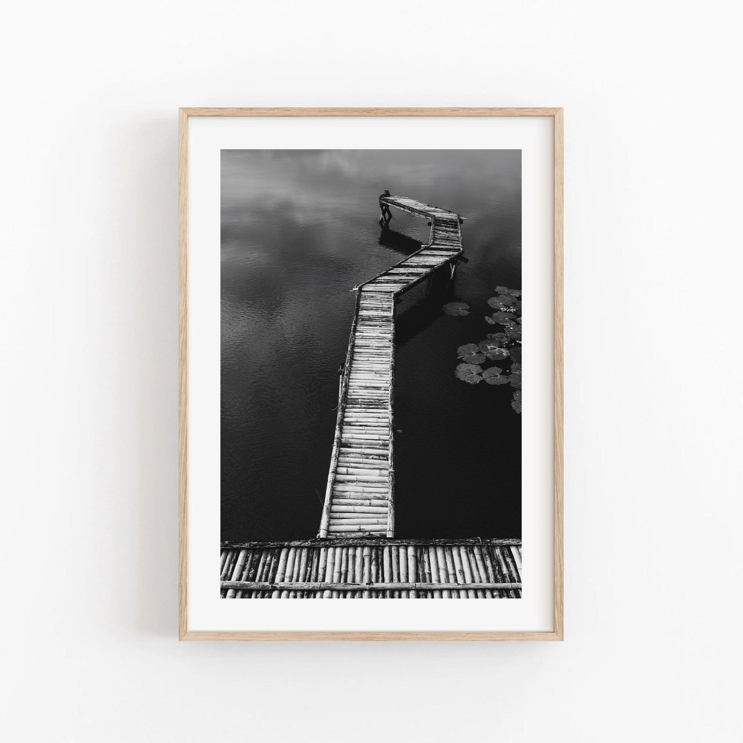 Bamboo Dock Black and White: A framed photo of a wooden pier extending into a serene body of water.