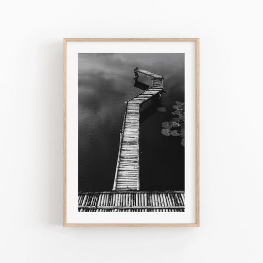 Bamboo Dock Black and White: A framed photo of a wooden pier extending into a serene body of water.