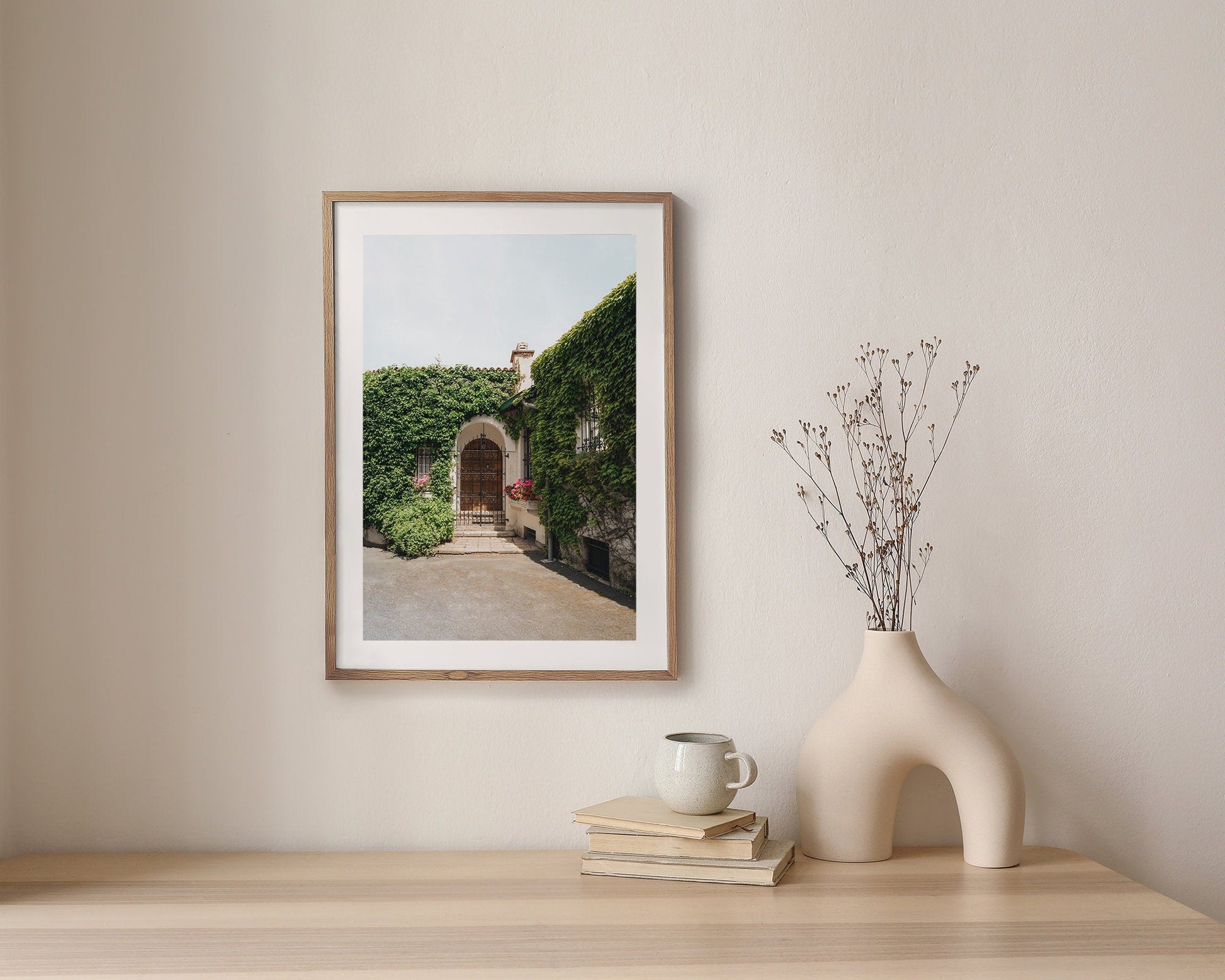 Basque Oasis: A framed photo of an ivy-covered house above a wooden table with a sculpted vase and mug.