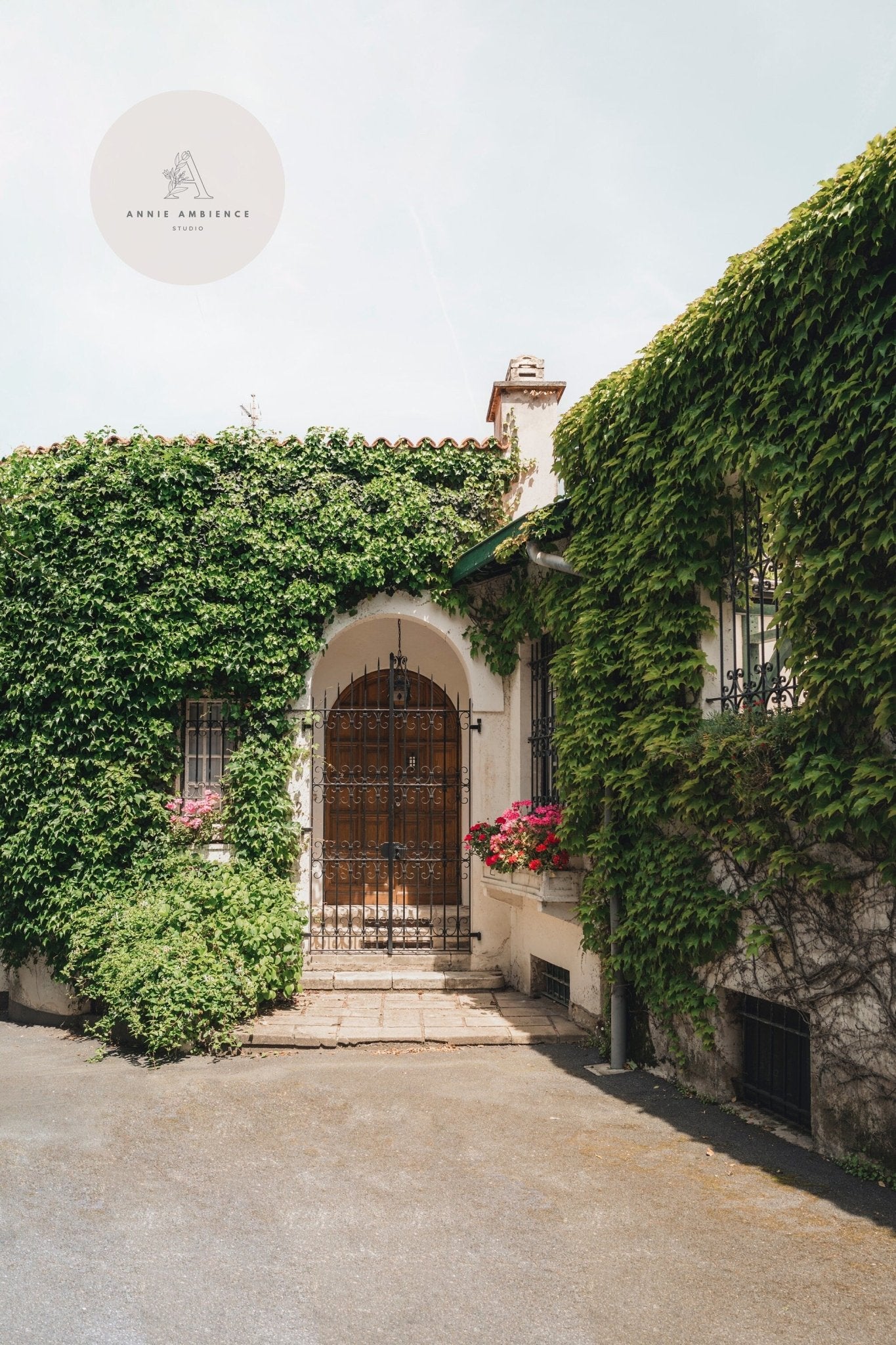 The Basque Oasis: A wooden door framed by ivy and pink flowers in sunlight, with a logo in the upper left corner.