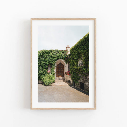 A framed photo of Basque Oasis hangs on a white wall, showcasing an ivy-clad building and an arched wooden door.
