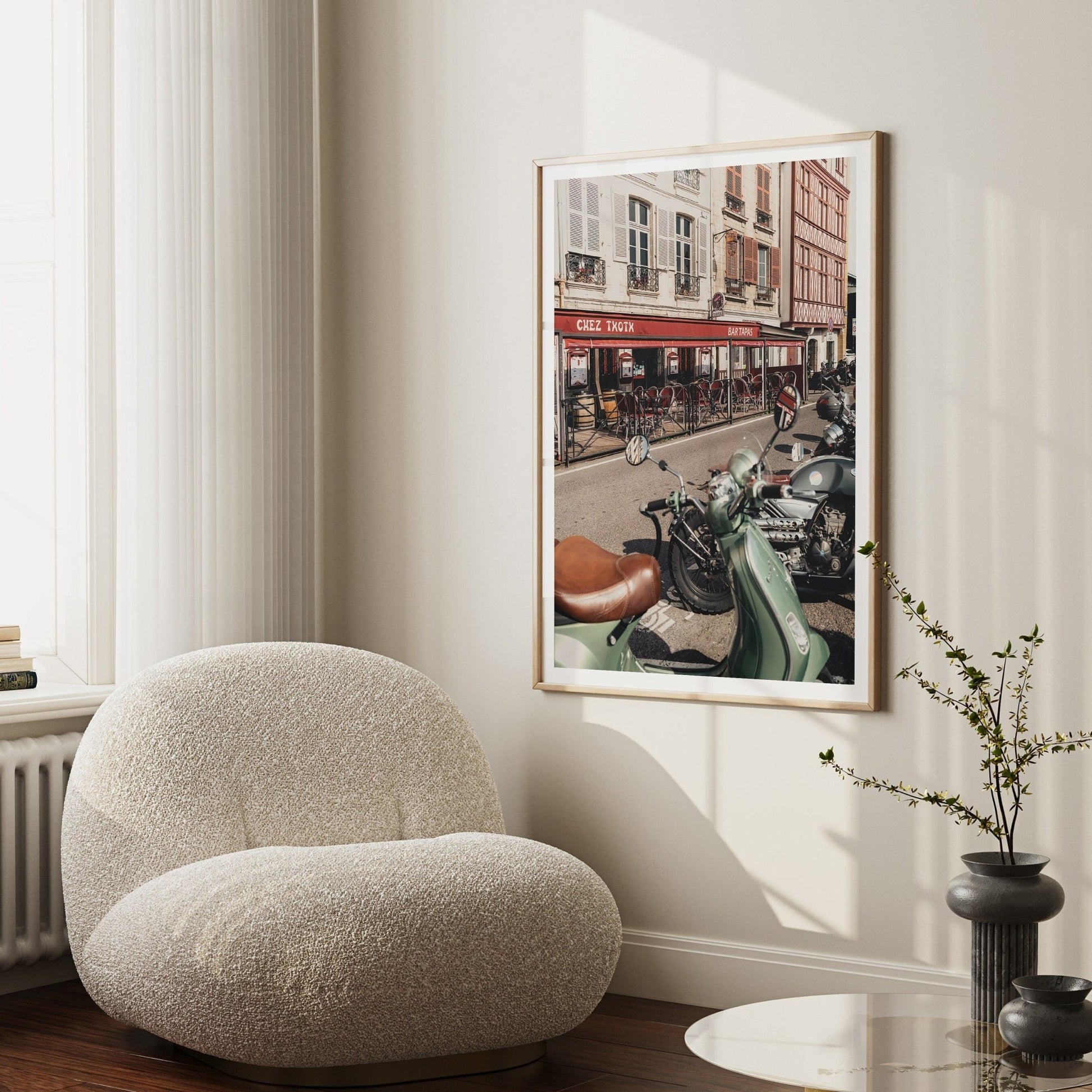 Cozy living room with a plush chair, modern side table, and Bayonne Vespa artwork depicting bikes and a café scene.