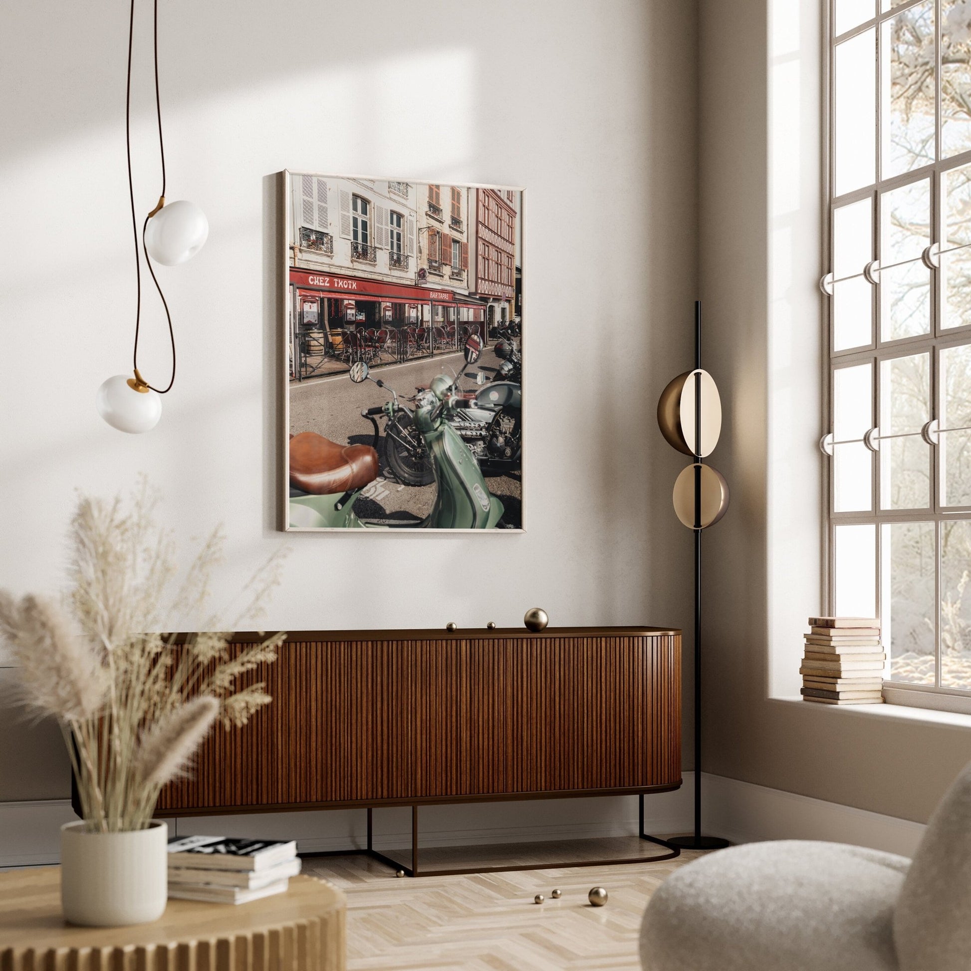 A modern living room features a Bayonne Vespa sideboard, hanging light fixture, window, and framed street photo on the wall.