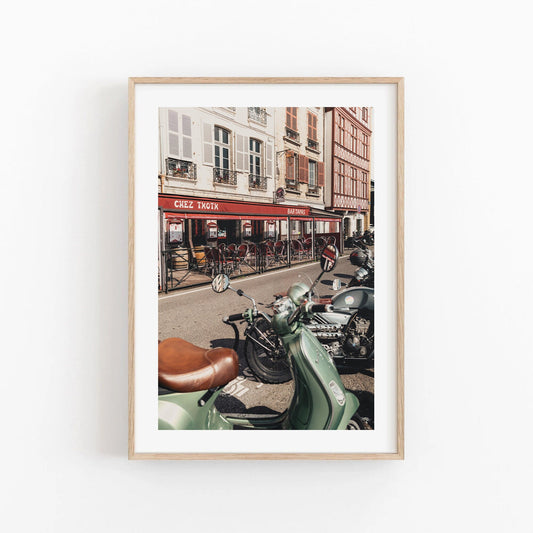 Framed photo Bayonne Vespa: street with parked scooters in front of a café with a red awning and outdoor seating.