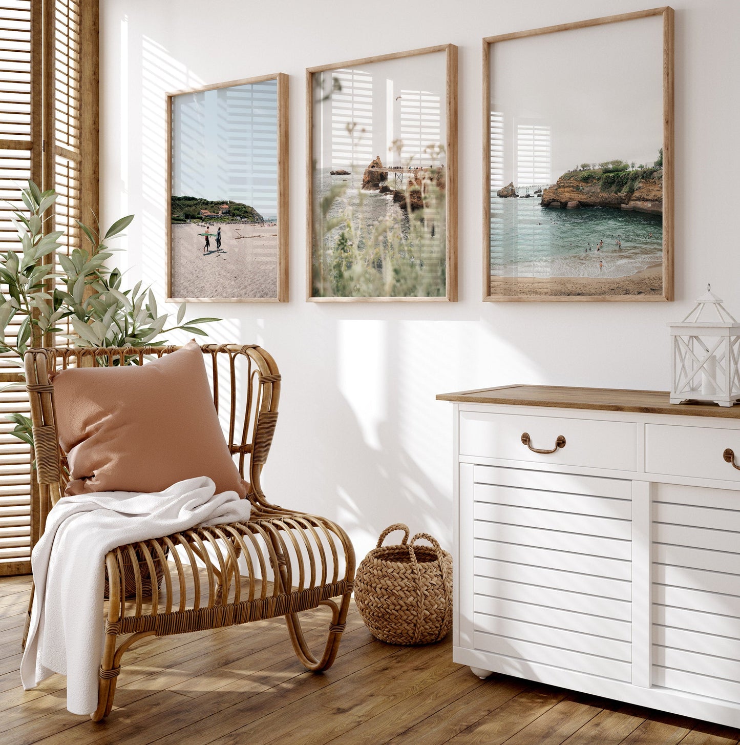A cozy room with a wicker chair, beige pillow, and Biarritz - Set of 3 coastal paintings in natural sunlight.