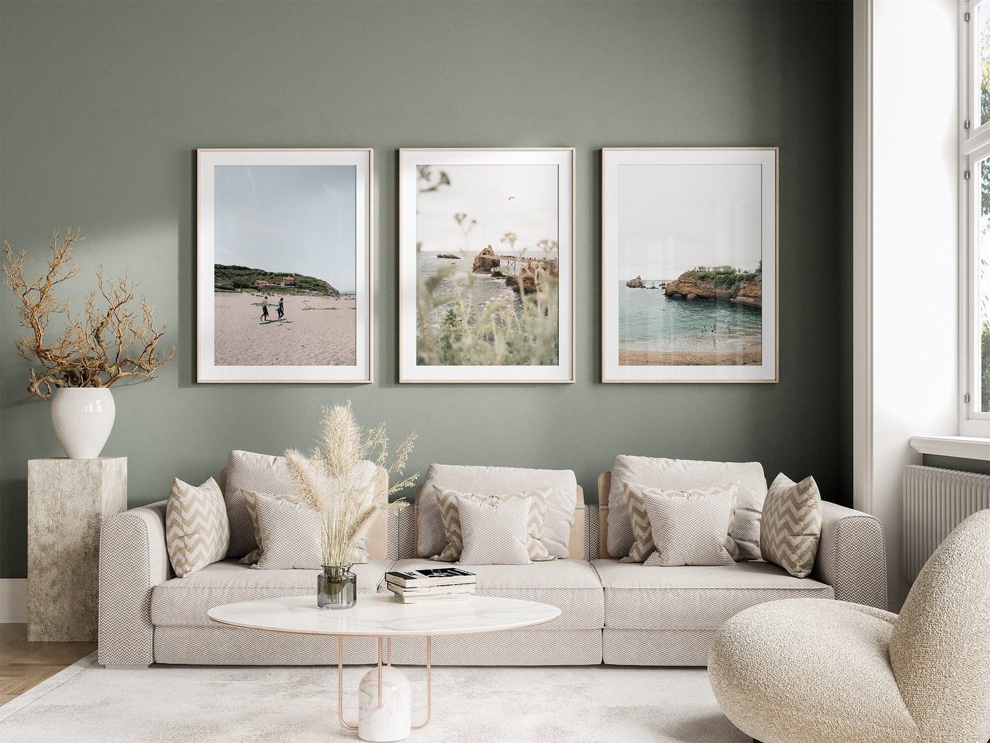 A cozy living room with a beige sofa, round coffee table, and the Biarritz set of 3 framed nature photos on a green wall.