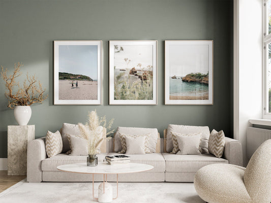 A cozy living room with a beige sofa, round coffee table, and the Biarritz set of 3 framed nature photos on a green wall.