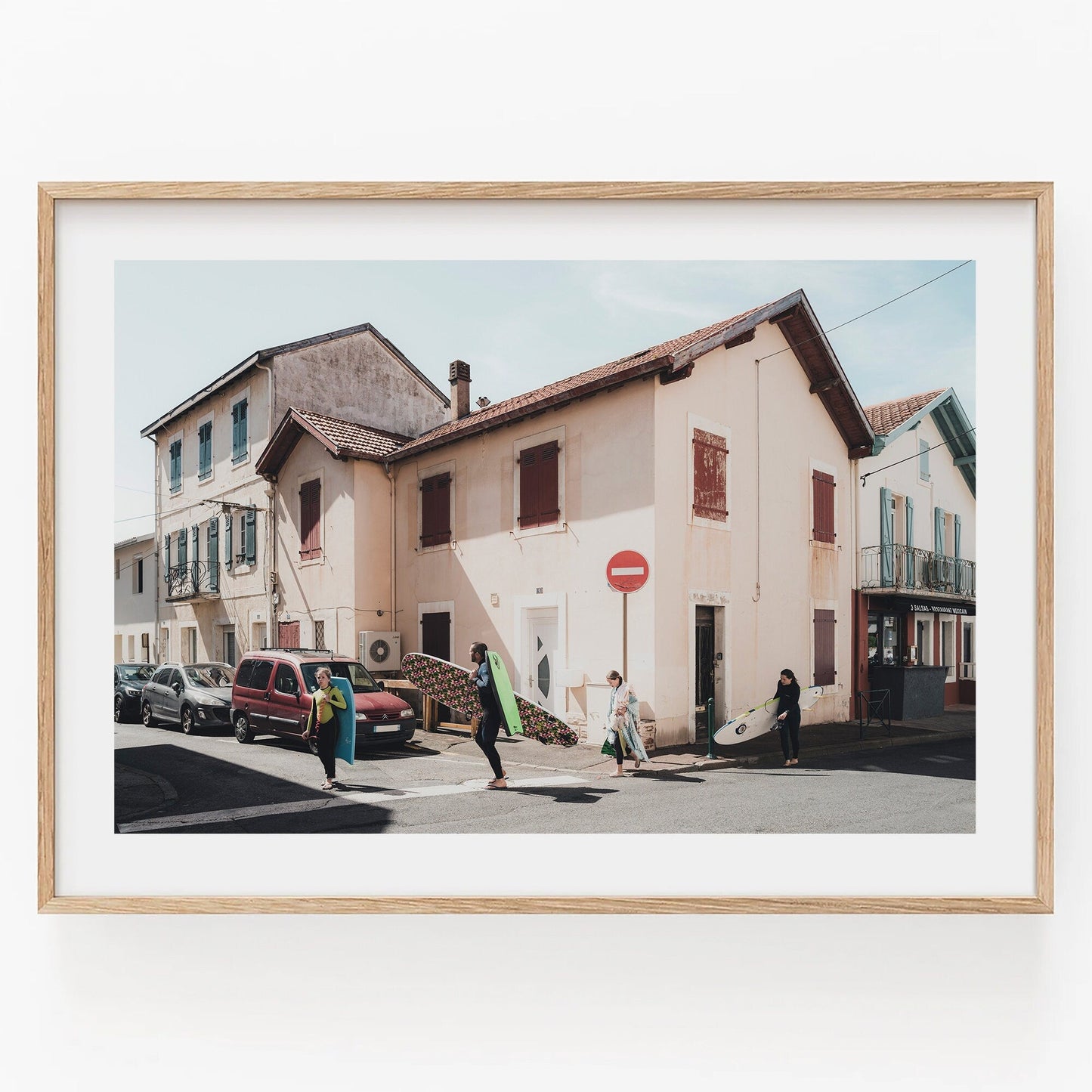Framed Biarritz Surfers photo of people with surfboards on a sunny street with white houses and parked cars.