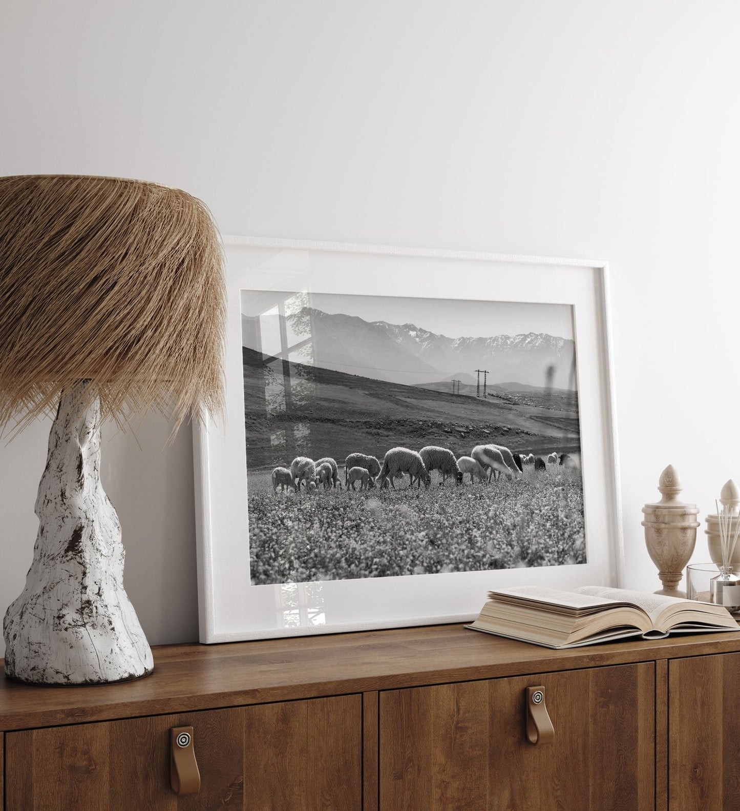 A framed Atlas Mountains I Black and White photo sits on a wooden cabinet beside a rustic lamp and an open book.