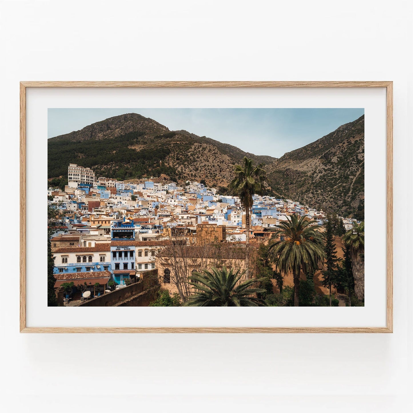 Framed photo titled Blue City Mountains showing a hillside town with blue buildings, palm trees, and mountains.
