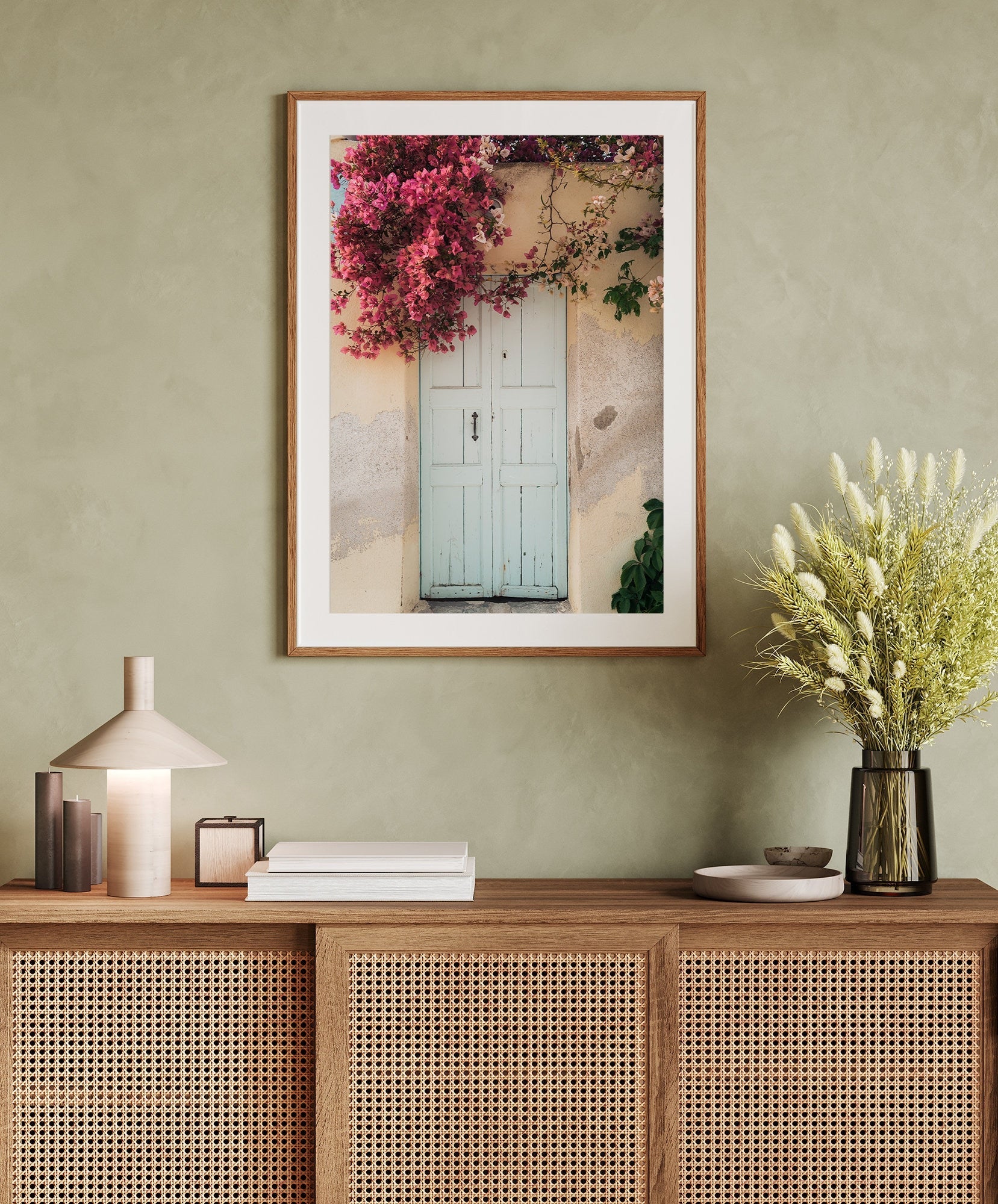 A framed Blue Door Bougainvillea photo hangs above a wicker console, adorned with books and a lamp.