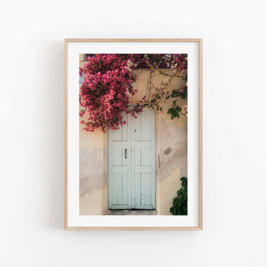 Framed Blue Door Bougainvillea photo on a textured wall with vibrant pink flowers cascading above.