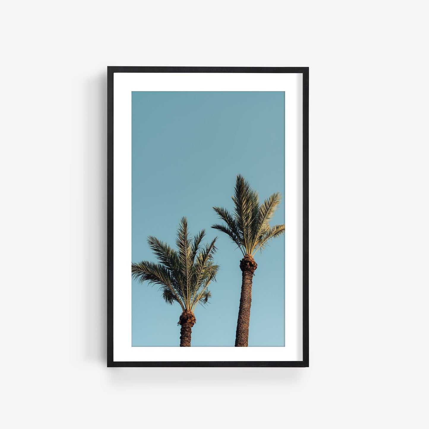 Framed Blue Sky Palm photo of palm trees against a blue sky, hung on a white wall.