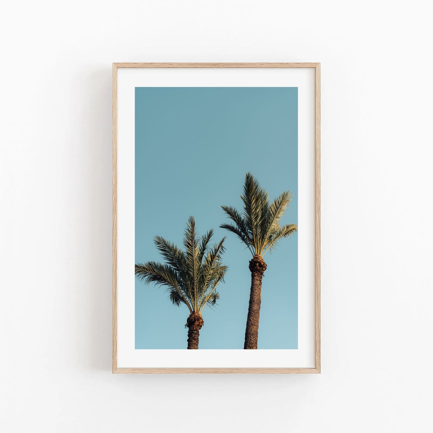 Framed photo titled Blue Sky Palm features two tall palm trees against a clear, vibrant sky.