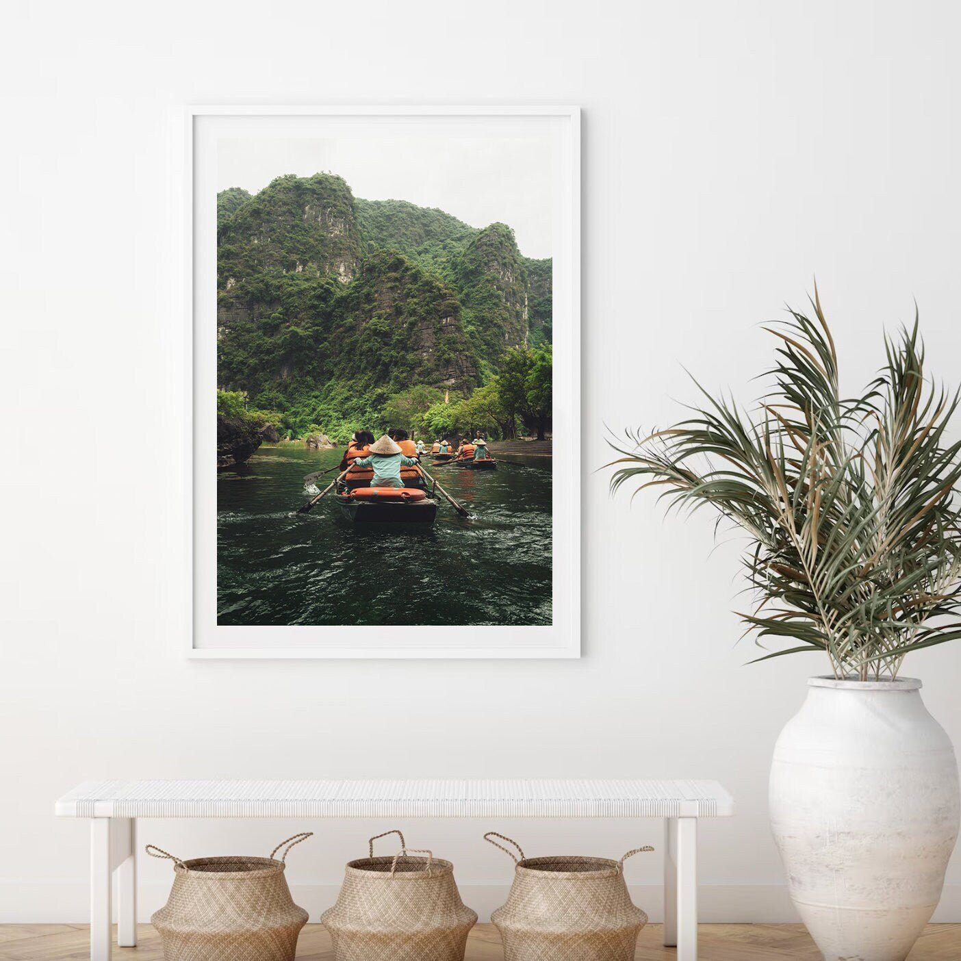 Boat Row framed photo: people rowing on a river with lush cliffs, displayed above a white bench and vases.