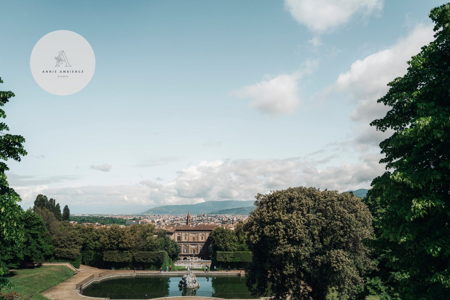 A scenic view of Boboli Gardens with a pond, a historic building, and a distant cityscape under partly cloudy skies.