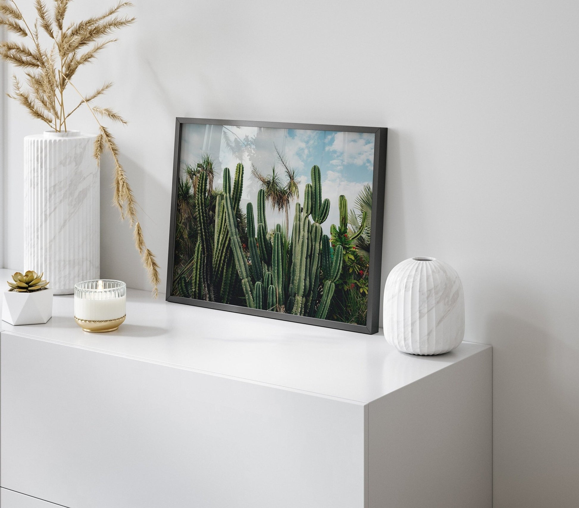 Framed Cactus Oasis photo on a minimalist white cabinet with vases and a small plant in a modern room.