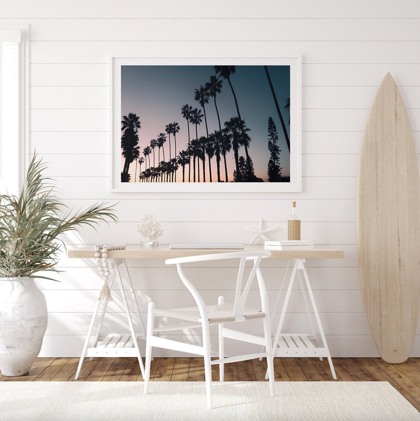 A coastal-themed room with California Dreams art, white chairs, a surfboard, and a potted plant.
