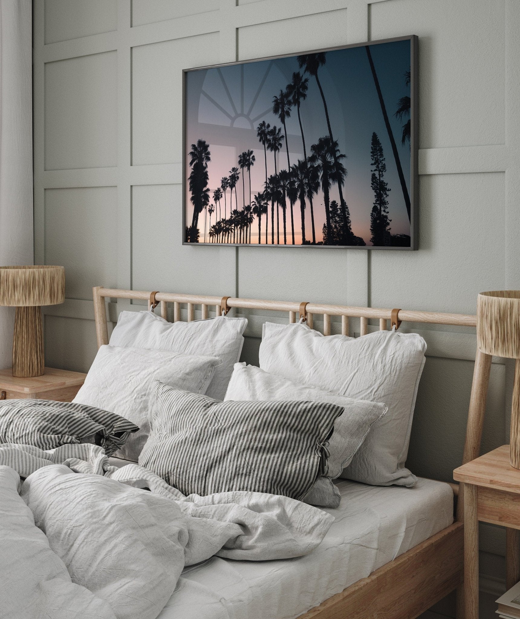 Cozy bedroom with a wooden bed, white bedding, and a California Dreams wall-mounted picture of palm trees at sunset.