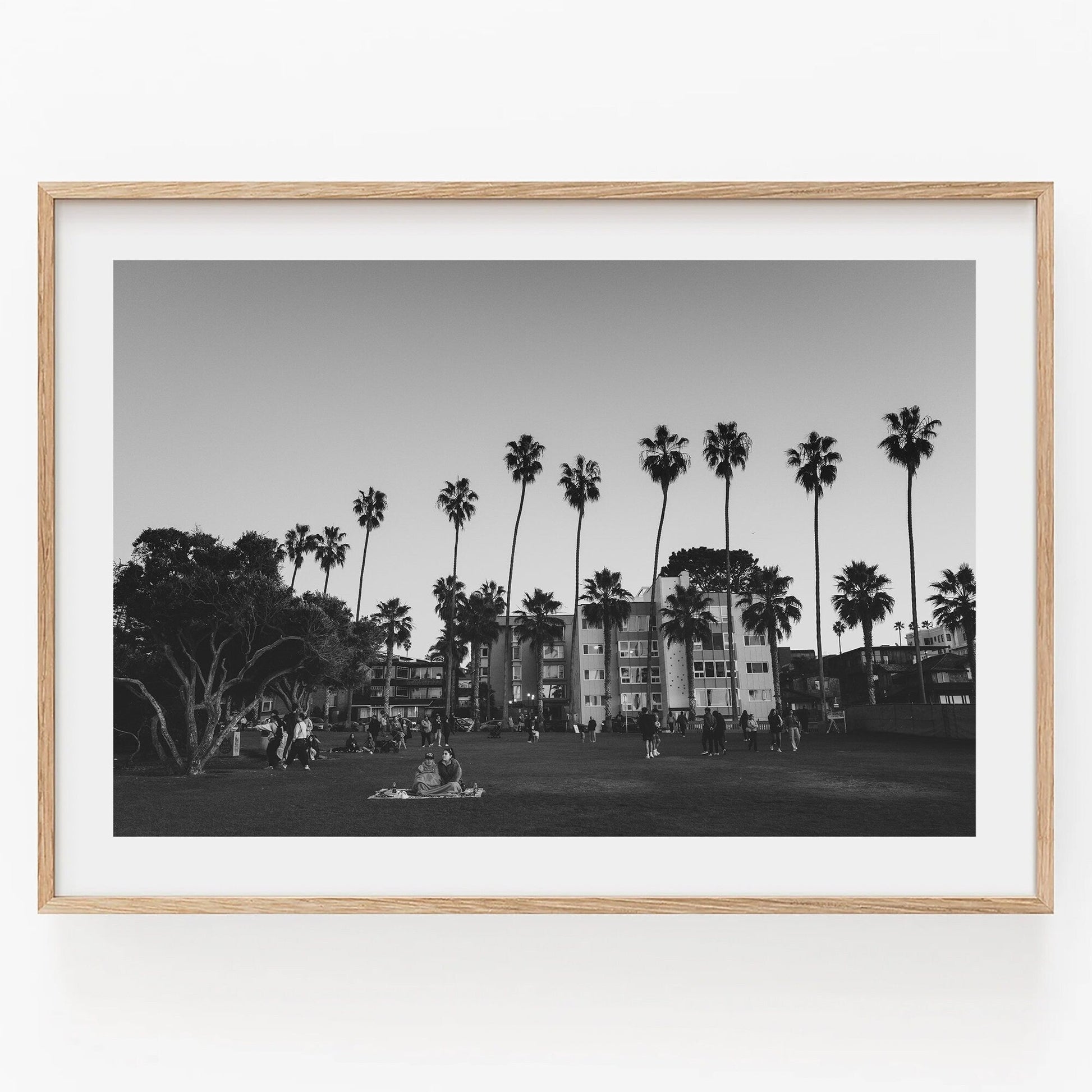 Black and white photo titled California Evening shows people relaxing on a grassy area with palm trees and buildings.