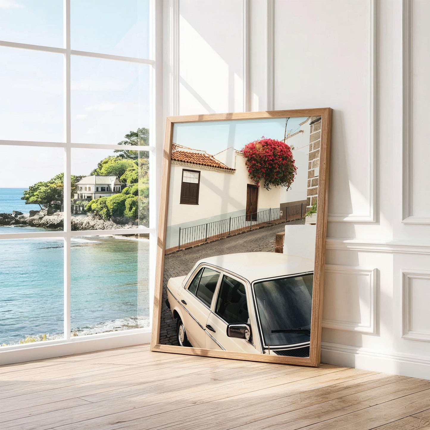 Classic in Bloom, a framed photo of a vintage car on a street, leans against an ocean-view window.