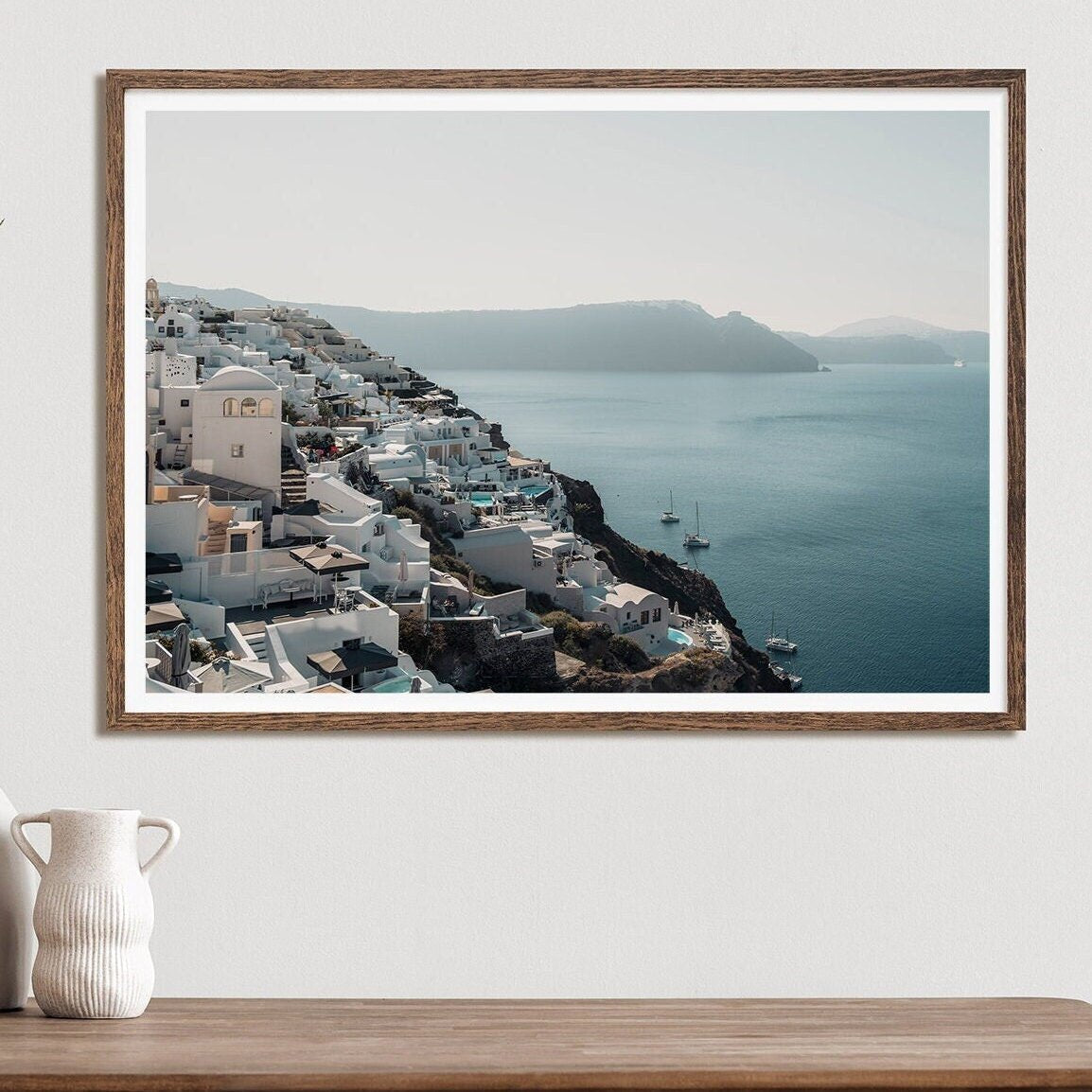 Cliffside Village framed photo shows a coastal scene with white buildings by a calm sea, displayed on a white wall.