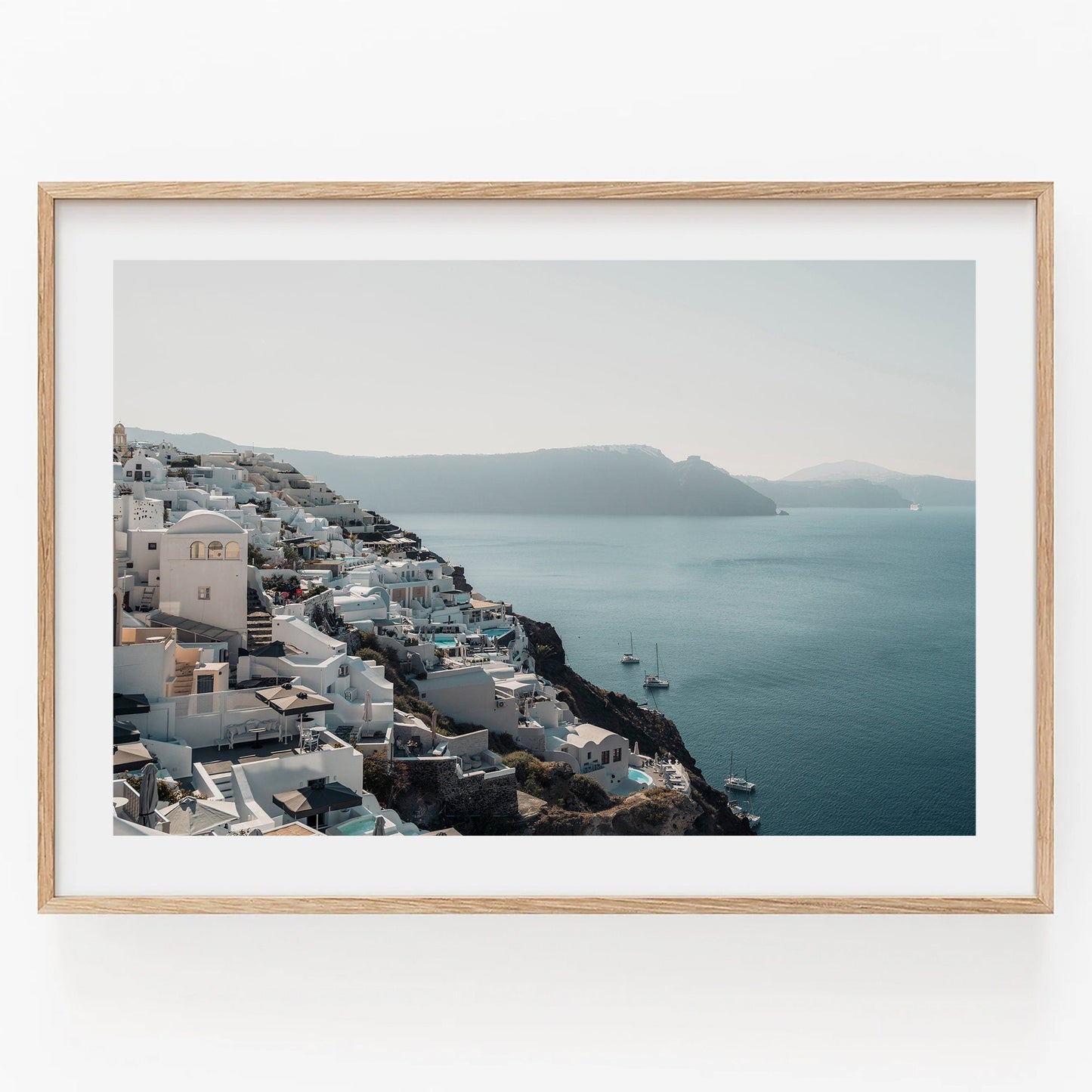 Framed photo of Cliffside Village with white buildings on a cliff overlooking a calm blue sea.