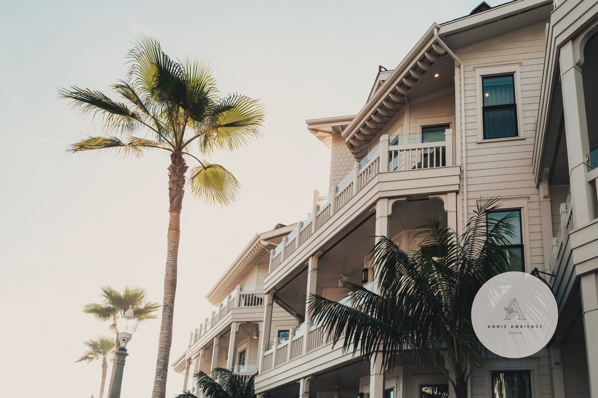 Beachfront hotel Coastal Abode features palm trees, balconies, and a bright sky with a nearby lamp post.