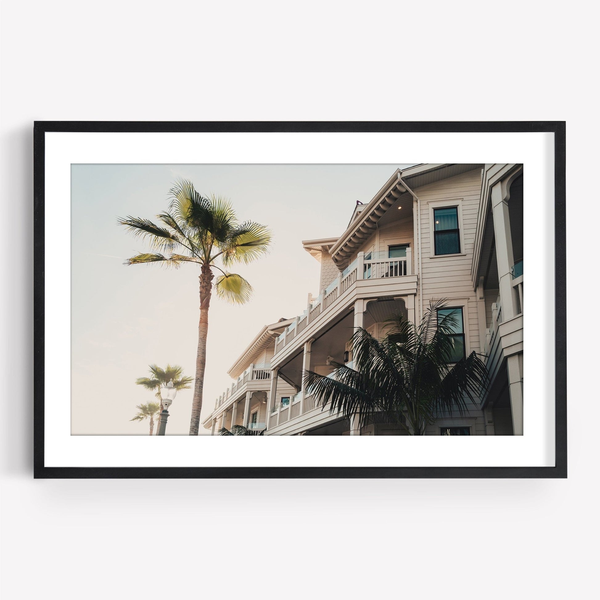 Coastal Abode: Framed photo of palm trees and a beige multi-story house with balconies under a clear sky.