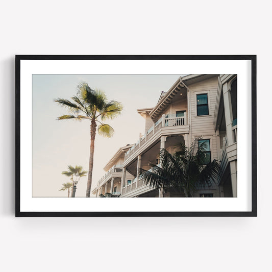 Coastal Abode: Framed photo of palm trees and a beige multi-story house with balconies under a clear sky.