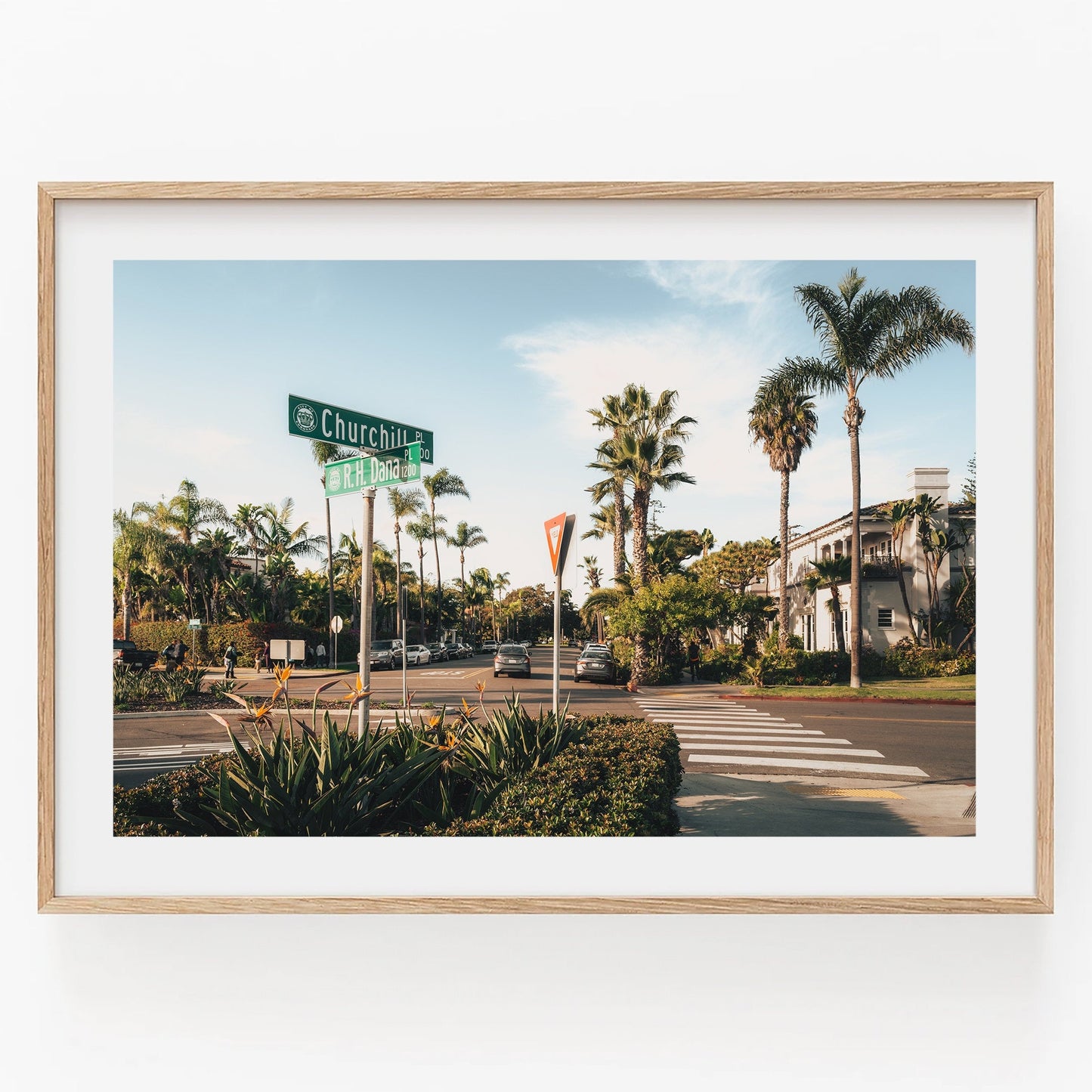 A street intersection with palm trees and cars, featuring a Churchill St. sign in a wooden frame from Coronado Crossing.