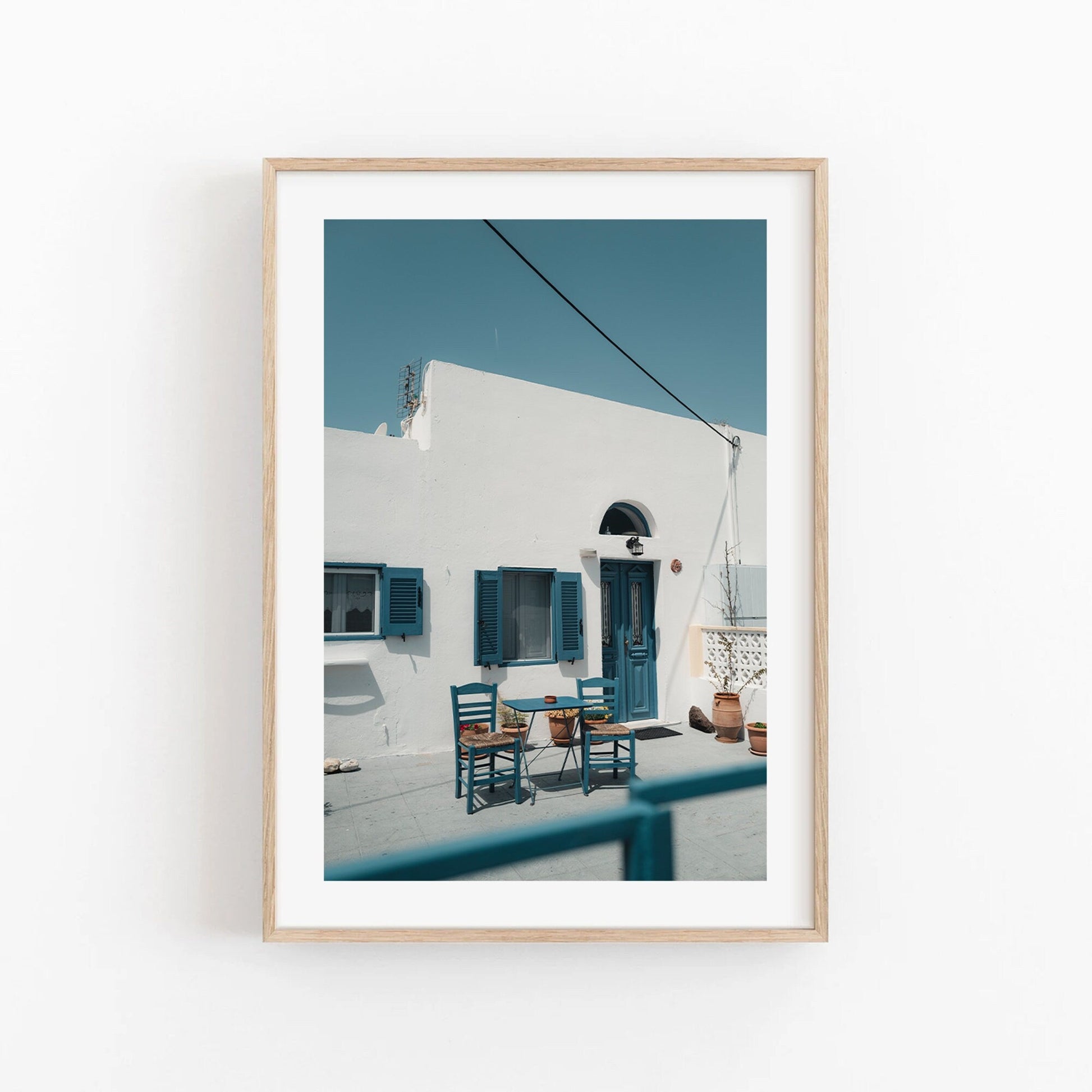 Framed Cozy Haven photo: white building with blue shutters, doors, and outdoor set of two chairs with a table.