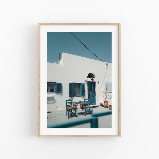 Framed Cozy Haven photo: white building with blue shutters, doors, and outdoor set of two chairs with a table.