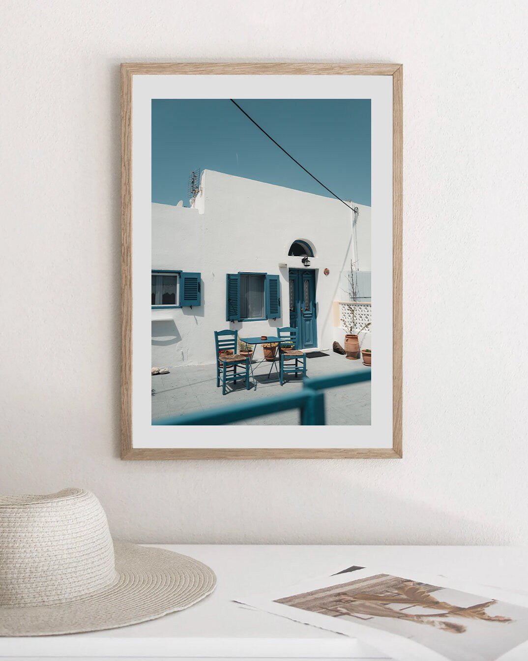 Cozy Haven framed photo of a Mediterranean house with blue accents near a hat and book.